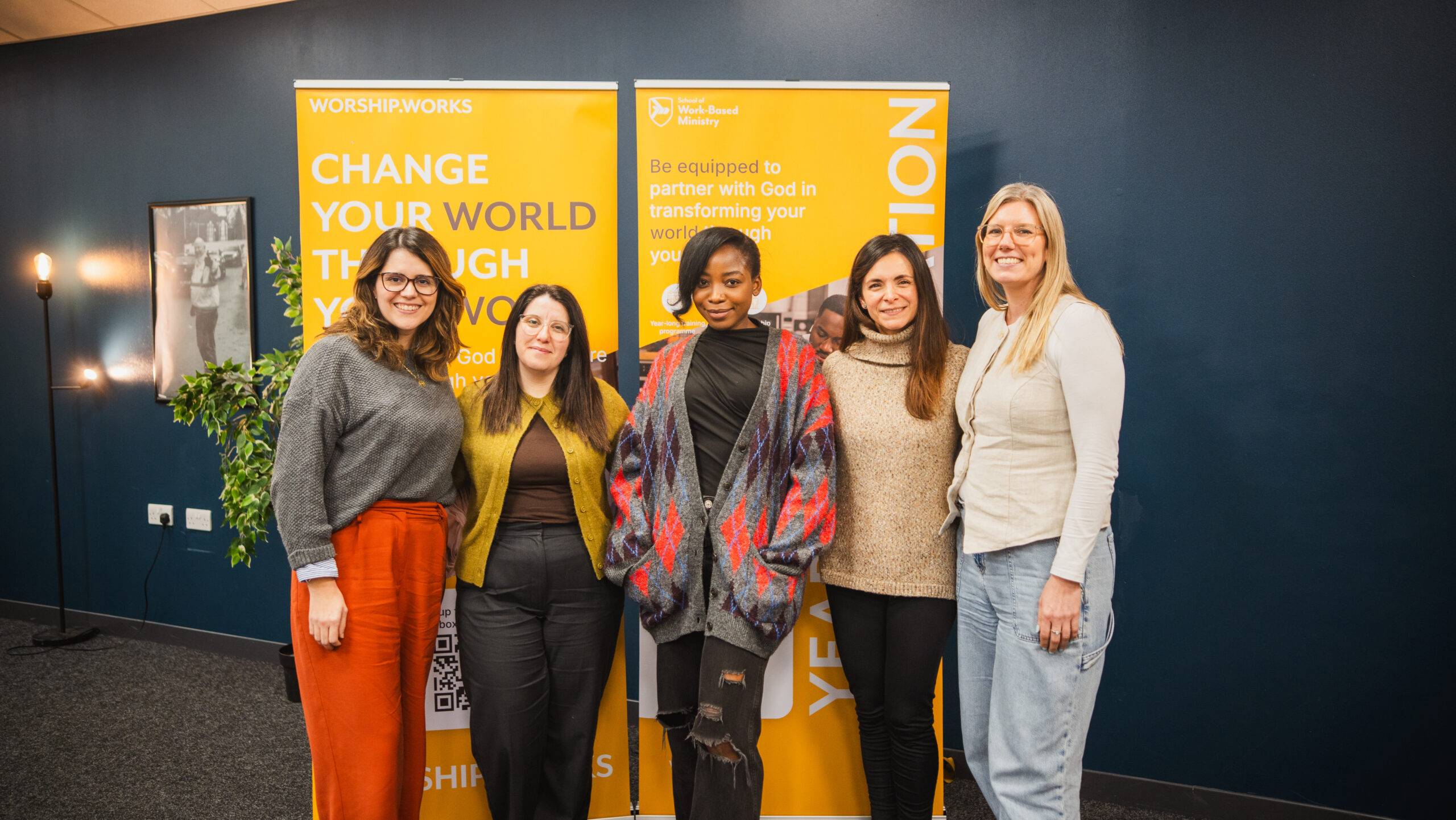Group of women smiling together in front of Worship.Works banners